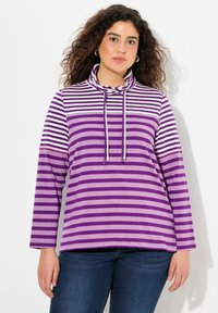 Maglietta a maniche lunghe a righe viola con collo a cowl e coulisse. Il materiale è morbido e presenta ampie righe orizzontali in diverse tonalità di viola.