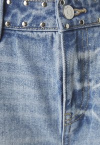 Světlá modrá džínovina s kovovými nýty, knoflík označený "ONLY" a viditelné švy na oděvu.