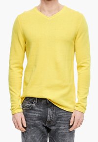Maglione giallo a maniche lunghe con scollatura a V, realizzato in morbido tessuto a maglia, abbinato a jeans grigio scuro, che evidenziano una vestibilità rilassata e un tessuto texturizzato.