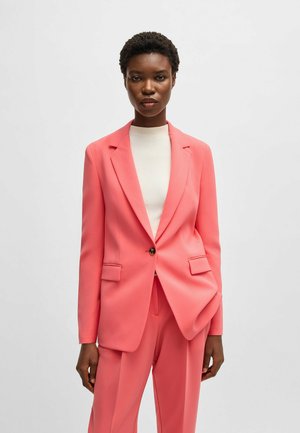 Pink tailored blazer with a single button, notch lapels, and two front pockets, paired with a fitted white ribbed top. Smooth texture.