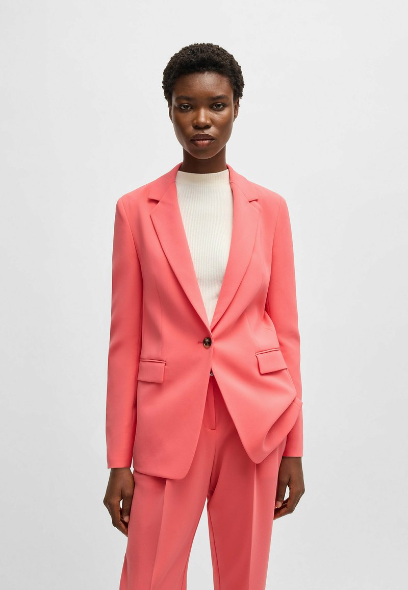 Rosa skräddarsydd kavaj med en enda knapp, slagkrage och två framfickor, tillsammans med en åtsittande vit ribbad topp. Slät textur.