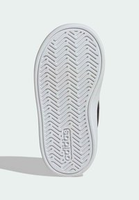 Bijeli đon tenisice s uzorkom riblje kosti, lagano zakrivljen prema nožnom prstu i utisnutim logotipom blizu pete.