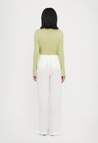 Light green ribbed sweater with long sleeves paired with white wide-leg trousers featuring front pockets and a smooth waistband.
