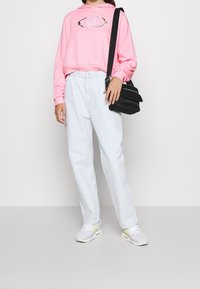 Rosa kortärmad sweatshirt med "Nike"-logotyp, ljusblå högmidjade jeans och grå sneakers med gula accenter, tillsammans med en svart axelväska.