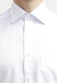 Valkoinen puuvillapaitapusero, jossa on klassinen kaulus, napitus edessä, yksi rintatasku ja sileä rakenne. Neljä nappia näkyvissä.