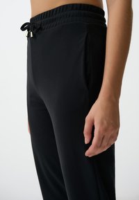 Schwarze, leichte Jogginghosen mit einem elastischen Bund und Kordelzug. Verfügt über Seitentaschen und eine glatte, weiche Textur.