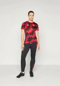 Rot und schwarz gemusterte Fußballtrikot mit Rundhalsausschnitt und Logo, kombiniert mit schwarzen Leggings mit roten Seitenstreifen.