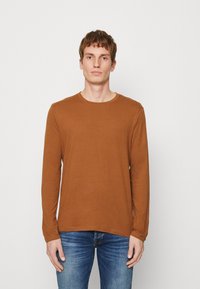 Langermet brun skjorte laget av mykt stoff med rund hals, sammen med blå jeans. Enkelt design, ingen synlige mønstre eller dekorasjoner.