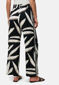 Pantaloni larghi bianco e nero con motivo a foglia, vita elastica e dettaglio a striscia laterale. Tessuto morbido con una texture fluida.