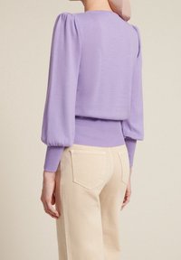 Lavendelkleurige gebreide trui met opgeblazen mouwen en een geribde zoom, gecombineerd met lichtbeige hoge taille broek, achteraanzicht.