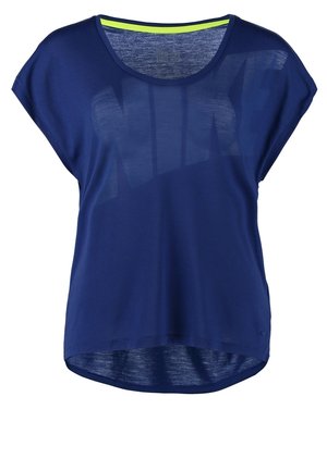 Femme portant un haut bleu ample, un pantalon gris clair raccourci et des baskets grises avec des semelles roses, marchant avec une main dans la poche.