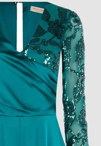 Abito da sera turchese con scollo a V profondo, corpo in raso e maniche lunghe trasparenti con ricamo floreale di paillettes. Lo scollo presenta un'apertura verticale.