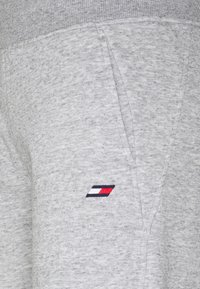 Jasnoszare spodnie dresowe wykonane z miękkiego materiału, z rypsowym pasem. Zawierają małe, wielokolorowe logo z boku.