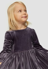 Paarse fluwelen jurk met lange mouwen, voorzien van een geplooide onderkant. Zachte textuur en ronde halslijn, geschikt voor kinderen.