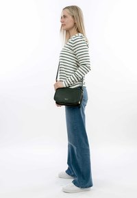 Černá kožená crossbody taška s texturovaným povrchem, obdélníkového tvaru, se zlatými kovovými detaily a nastavitelným popruhem, kterou nese žena v pruhovaném topu.