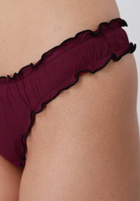 Μπορντό κάτω μέρος μπικίνι με μαύρη βολάν περιφέρεια, ελαστική μέση και απαλή υφή υφάσματος, με εφαρμογή που αγκαλιάζει το σώμα.
