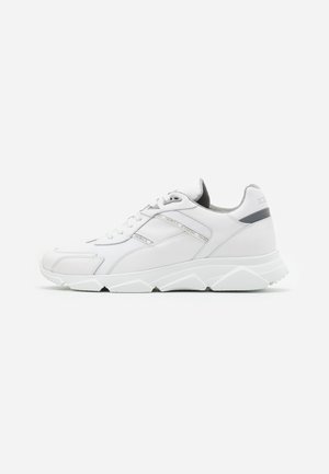 Biały niski sneaker z masywną podeszwą, z przodu na sznurowadła i szarą wyściółką wewnętrzną, pokazany z profilu na jednolitym tle.