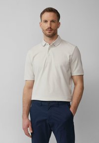 Polo beige avec un col classique et des manches courtes. Tissu en mélange de coton, avec une texture subtile et une patte de boutonnage à trois boutons.