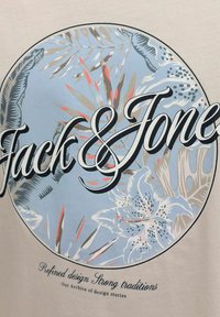 Motif floral circulaire aux tons bleus et beiges avec le texte "Jack & Jones" en surimpression et un texte plus petit indiquant "Design raffiné Fortes traditions."