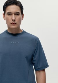 Blå kortärmad skjorta i mjukt tyg, med rund halsringning och diskret logotyptryck i mitten.