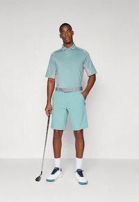 Golfiriietus, mis koosneb helesinisest polo särgist hallide detailidega ja sobivatest lühikestest pükstest, mida täiendab hall vöö ja valged golfijalatsid.