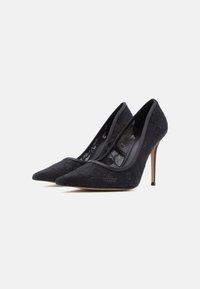 Escarpins noirs en dentelle à talons hauts avec bouts pointus, intérieur lisse et talons aiguilles fins, ornés d'un motif floral à l'extérieur.