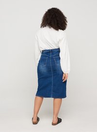Denim midi krilo v temno modri barvi, visoko pasu z oprijetim krojem. Zadnji del ima dva žepa in subtilno zbledelost; kombinirano z belo majico.