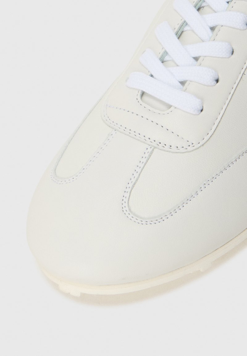 Close-up van een witte leren sneaker met witte veters en gedetailleerde stiksels op de teen en het bovenste gedeelte.