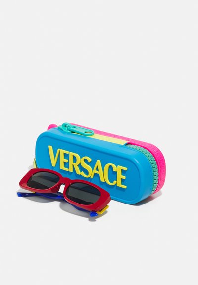 Sunglasses with red frame and blue accents, paired with a bright blue case featuring yellow "VERSACE" logo and multicolored zipper.