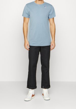 Hellblaues Baumwoll-T-Shirt mit Rundhalsausschnitt und kleinem Logo, kombiniert mit schwarzen Hosen und weißen Turnschuhen mit orangefarbenen Akzenten.