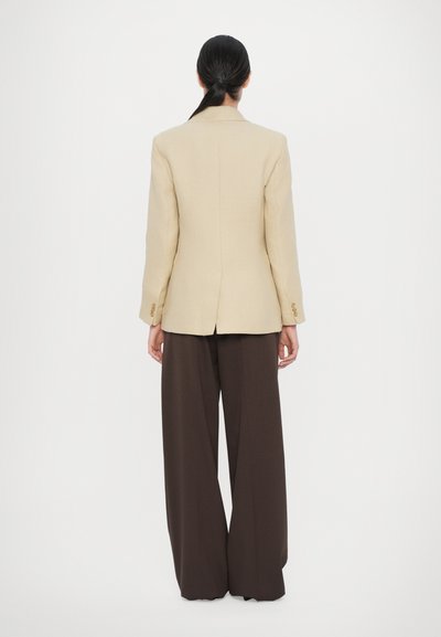 Beige blazer with a fitted shape and buttoned cuffs, paired with wide brown trousers; smooth texture, minimal seams, and no visible patterns.