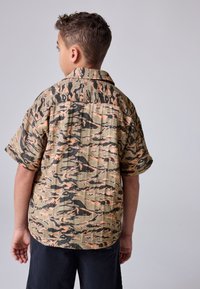 Korte mouwen shirt met een camouflagepatroon in kaki, zwart en oranje tinten. Lichtgewicht, met een ontspannen pasvorm en een kraag.