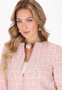 Helle rosa Tweedjacke mit strukturiertem Gewebe, das mehrfarbige Einsprengsel aufweist, kragenloser Gestaltung und einem großen Perlenhalsband als Akzent.