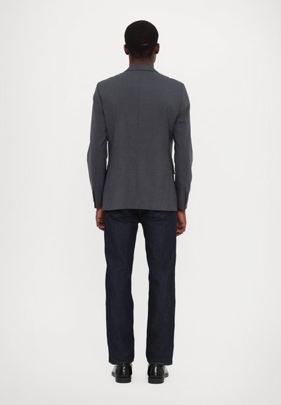 Grauer tailorierter Blazer mit einem Schlitzausschnitt, kombiniert mit dunklen Jeans. Der Blazer verfügt über einen Reverskragen und geknöpfte Manschetten.