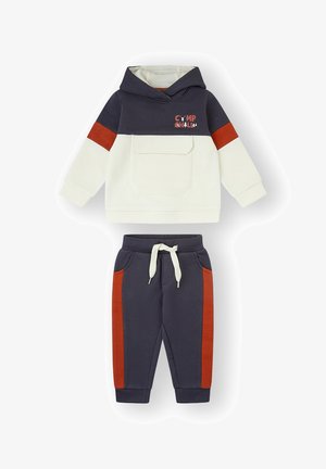 Sudadera con capucha para niño pequeño en azul marino y crema con bolsillo tipo canguro, acento rojo y pantalones deportivos con cordón, bolsillos laterales y rayas rojas. Material de algodón.