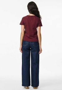 Mörkröd kortärmad topp med texturerad yta och vågformad nederkant, kombinerad med vida mörkblå jeans. Synliga bakfickor och avslappnad passform.