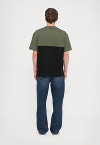 Tricou cu mânecă scurtă, secțiune superioară verde și secțiune inferioară neagră. Materialul este bumbac; finisaj texturat. Partea din spate are un logo aproape de guler.
