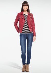 Chaqueta de motociclista de cuero rojo con detalles acolchados en los hombros, llevada sobre una camiseta de rayas en blanco y negro, combinada con jeans ajustados azules y botas de tobillo en color marrón claro.