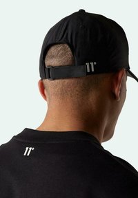 Gorra de béisbol negra con correa ajustable que presenta un logo plateado "11°" en la parte posterior. Fabricada con un tejido suave y con una forma estructurada.