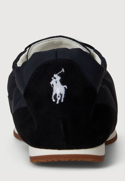Scarpa da ginnastica blu navy con tomaia in morbido suede, foderata in bianco e con un logo ricamato bianco di un giocatore di polo sul tallone. Suola in gomma marrone.