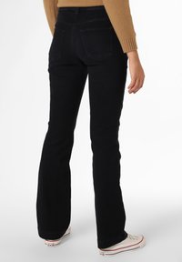 Czarne dżinsy typu dzwony, wykonane z denimu, z tylnymi kieszeniami, dopasowaną talią i podwiniętymi nogawkami, w połączeniu z białymi trampkami z płótna.