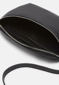 Czarna skórzana torebka kopertówka z zamknięciem na zamek, wewnętrzną kieszonką, gładką teksturą i cienkim paskiem. Wnętrze wyłożone ciemnym materiałem.