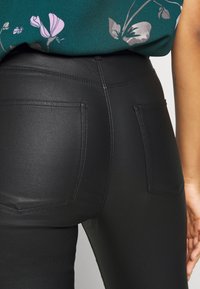 Pantalones de cuero ecológico negros con una textura suave, que cuentan con dos bolsillos traseros y una cinturilla alta. Los detalles cosidos aportan definición.
