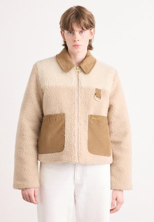 Zandkleurige en beige fleecjacket met corduroy zakken, kraag en gouden hardware. Beschikt over een ritssluiting aan de voorkant en een decoratieve lus.