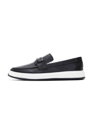 Scarpe slip-on in pelle nera con profilo basso, finitura testurizzata, suola in gomma bianca a contrasto e una cintura decorativa sul davanti.