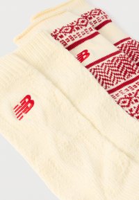 Πλεκτές κάλτσες σε εκρού χρώμα με υφασμένη υφή και κόκκινες λεπτομέρειες. Η μία κάλτσα έχει γεωμετρικό σχέδιο, ενώ η άλλη διαθέτει λογότυπο και πλεκτή υφή με καλώδιο.