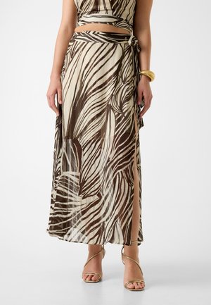 Gonna maxi a righe marroni e crema con spacco laterale, realizzata in tessuto leggero, con vita annodata e design fluente. Accenti dorati sui piedi.