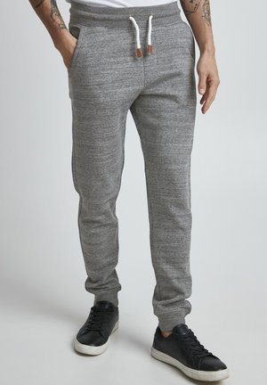 Gray cotton joggers with a tapered fit, featuring a drawstring waist with leather accents and side pockets. Black sneakers are worn.