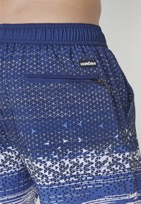 Námornícke šortky so geometrickými modro-bielymi trojuholníkovými vzormi, elastický pás a bočná vrecko na zips. Zobrazená značka.