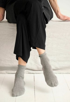 Sivé rebrované ponožky strednej dĺžky z mäkkej látky, doplnené o čierne voľné nohavice, sediace na svetlom pozadí.